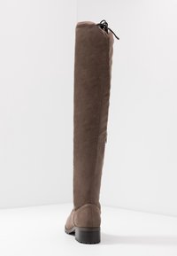 Bota de ante marrón sobre la rodilla con un diseño recto, tacón bajo y cremallera trasera. Textura suave, sin patrones visibles ni detalles de metal.