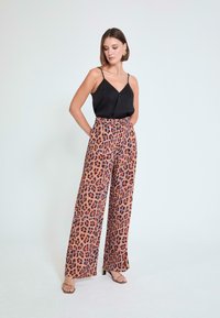 Camisola de satén negra combinada con pantalones de talle alto y pierna ancha con estampado de leopardo en naranja, marrón y púrpura oscuro.