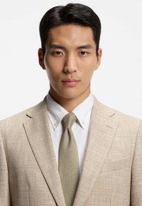 Giacca da completo a quadri beige con camicia bianca con colletto e cravatta grigio chiaro. Tessuto liscio, vestibilità sartoriale e dettagli netti del rever.