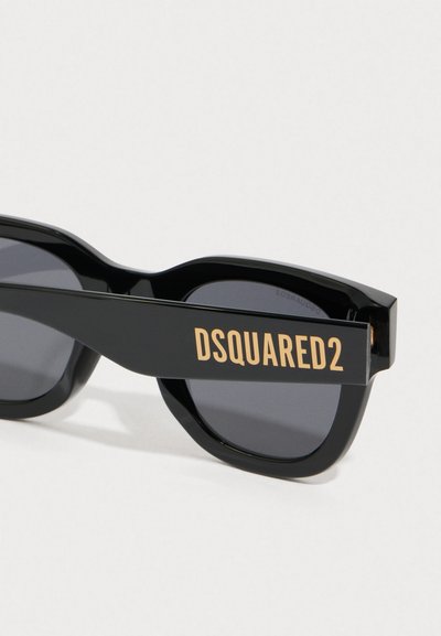 Črne sončna očala z masivnim dizajnom. Sive leče in drzen, zlat "DSQUARED2" logo na strani. Gladek plastični material.
