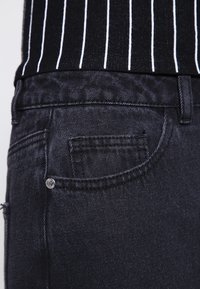 Černé džíny z denimu s zadní kapsou se švy a kovovou nýtkou. Materiál má měkkou texturu a mírnou pružnost.