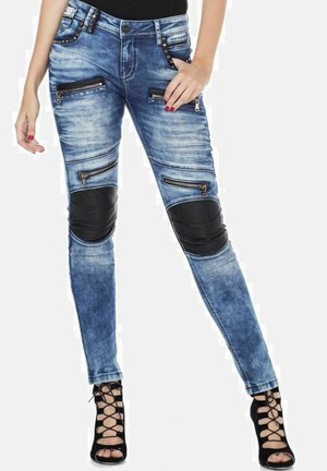 Blaue Jeans aus Denim mit mehreren Reißverschlusstaschen, schwarzen Kunstlederknieflicken und Nietenakzenten am Bund. Enganliegendes Design.