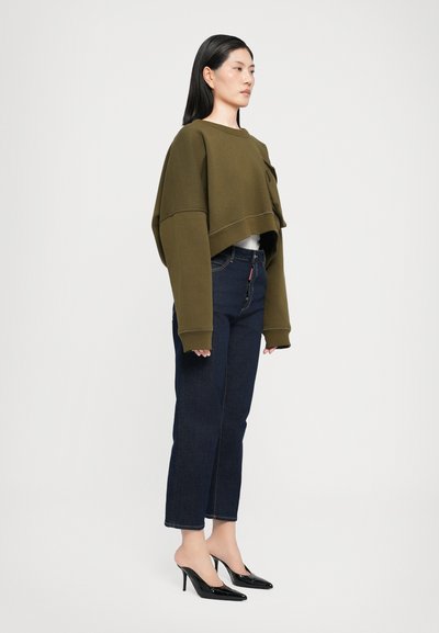 Felpa cropped verde oliva, jeans blu scuro e scarpe con tacco nere. Presenta maniche ampie e una vestibilità rilassata.