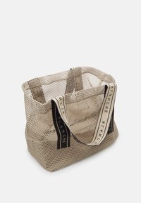 Beige Netz-Einkaufstasche mit schwarzen Stoffgriffen. Rechteckige Form, offener oberen Teil, mit dezenter Markenbeschriftung auf den Griffen. Strukturierte Oberfläche.