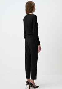 Zwarte top met lange mouwen en geribbelde textuur, gecombineerd met zwarte getailleerde tapered broek, gedragen met zwarte pointed-toe hoge hakken.