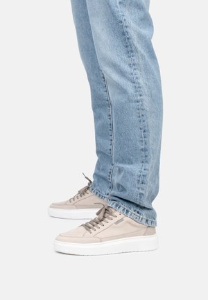 Beige Wildlederschuhe mit niedrigem Profil, runder Spitze und weißer Gummisohle, kombiniert mit hellblauen geraden Jeans.
