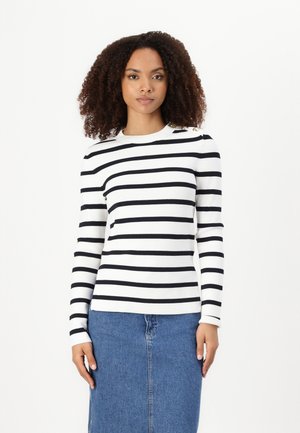 Long-sleeve striped top in white and black with a crew neckline and decorative buttons on the shoulder. Paired with a denim skirt.