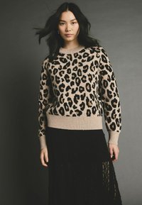 Beige Pullover mit Leopardenmuster, ausgestattet mit einem gerippten Halsausschnitt und Bündchen, kombiniert mit einem schwarzen, schichtweisen Rock. Weiche Textur, Pullover-Design.