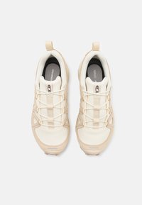 Beige athletic shoes with a textured mesh upper, reinforced synthetic overlays, and elastic laces. Features a pull tab at the heel.