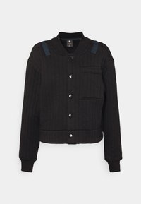 Svart quiltad jacka med kort skärning, som har krage, framknäppning med knappar och en ficka på vänster bröst med blå detaljer.