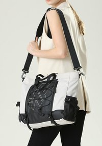 Grande borsa a spalla in grigio chiaro e nero, caratterizzata da una tracolla regolabile, inserti in gomma, tasche in rete e dettagli con cordino elastico.