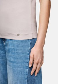 Hellrosa, gerippter Tanktop mit einem dezenten Logo-Akzent am Saum, kombiniert mit blauen Jeans aus Denim mit geradem Schnitt und strukturiertem Finish.