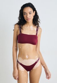 Bordo bikini set s pravokutnim bralet topom i donjim dijelom sa niskim strukom. Ima brendirane elastične trake i glatku, rastezljivu tkaninu.