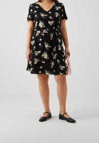 Robe noire à fleurs avec des manches courtes, un décolleté en V, une taille nouée et une jupe évasée. Présente des fleurs roses et des feuilles vertes sur un fond noir.