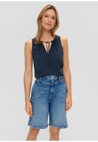 Blusa senza maniche di colore blu navy con scollo a V e dettaglio con fiocco, abbinata a pantaloni corti in denim blu a vita alta, con orlo sfilacciato.