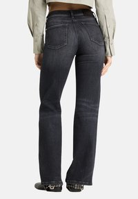 Dunkle, ausgestellte Jeans aus Denim mit fünf Taschen, leichtem Farbverlauf und tailliertem Schnitt. Verfügt über dekorative Nähte und einen strukturierten Bund.