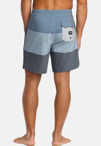 Modré a šedé plavky s pruhovaným vzorem, vybavené zadní kapsou, vyrobené z rychleschnoucího materiálu, s pohodlným střihem.