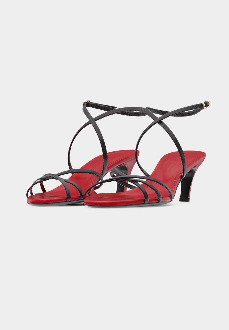 High-Heel-Sandalen mit roter Sohle, dünnen schwarzen Lederriemen, die über Zehen und Knöchel verlaufen, Schnallenverschluss und schlanken Absätzen.