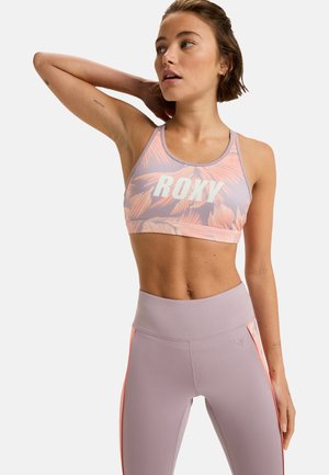 Sporty crop top with palm leaf pattern in pink and purple, featuring a bold white "ROXY" logo. Matched with high-waisted lavender leggings with orange accents.