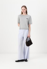 Maglione grigio a maniche corte, pantaloni a righe con gamba larga, mocassini neri e una piccola borsa marrone. Design semplice con accenti minimi.
