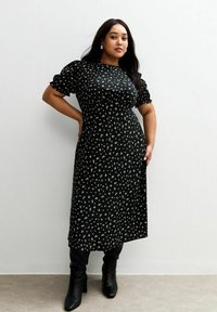 Vestido negro con estampado de flores, con mangas cortas abullonadas y largo hasta la rodilla, que presenta una cintura entallada y una tela suave y texturizada. Combinado con botas negras hasta la rodilla.