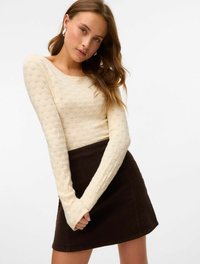 Top in maglia a maniche lunghe di colore crema, abbinato a una mini gonna in corduroy marrone scuro. Il top presenta un collo rotondo e maniche aderenti.
