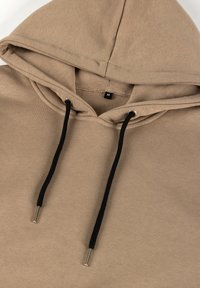 Beeži toonitud kapuutsiga dressipluus mustade nööridega ja keskmise suurusega sildiga, mis on nähtav krae sees.