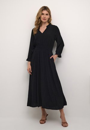 Black long-sleeve dress with a V-neck, elastic waistband, and side pockets. Made of textured fabric with a subtle check pattern.