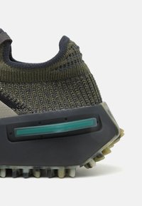 Sneakers med övre i mörkgrön och grå stickad textil, med en texturerad yta, rena linjer och en gummisula med geometrisk design.