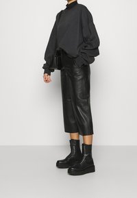 Svart oversized tröja i kombination med högmidjade svarta läderculotter och kraftiga svarta snörstövlar. Släta ytor, minimalistisk design.