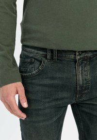 Vervaagde zwarte jeans met vijf zakken, een knoopsluiting en contrasterende stiksels, gecombineerd met een olijfgroene blouse met lange mouwen.