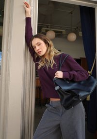 Juodas odinis tote krepšys su lygiu paviršium ir metaliniais akcentais; derinamas su giliu purpuriniu megztiniu ir pilkomis dryžuotomis kelnėmis.