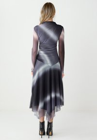 Sukienka z długim rękawem, dopasowaną górą i zwiewnym dołem, z gradientowym szarym odcieniem, miękką teksturą i przezroczystymi akcentami. Czarne botki na obcasie.