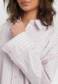 Light pink button-up shirt with green vertical stripes, featuring a classic collar and wide cuffs. Smooth fabric texture, standard fit.