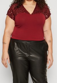 Top burdeos con mangas de encaje con lentejuelas y escote en V, combinado con pantalones de cuero sintético negros, que cuentan con una textura suave y cintura elástica.