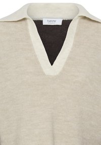 Pull en maille beige avec col ivoire et encolure en V, affichant une étiquette de la marque b.young à l'intérieur de l'encolure. Pas de personnes ni d'arrière-plan visible.