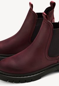 Botas Chelsea de cuero burdeos con paneles laterales elásticos, suela de goma negra y tiradores para un fácil ponérselas. Textura suave con detalles de costura.