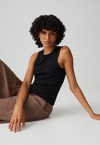 Schwarzes, geripptes Tanktop mit Rundhalsausschnitt, kombiniert mit braunen, weit geschnittenen Hosen. Der Stoff wirkt weich und hat eine körpernahe Passform.