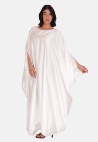 Witte satijnen kaftan jurk met een losvallende pasvorm, ronde halslijn en uitsparingen voor de armen. Glad textuur en lange lengte, gedragen met zwarte sandalen.