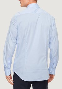 Camicia azzurro chiaro a maniche lunghe in cotone, con colletto a punta, polsini con bottoni e una vestibilità leggermente sagomata con orlo curvo.