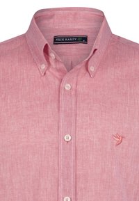 Camisa rosa claro de botones, hecha de tela texturada, con un cuello clásico y un logo de ave bordado en el lado izquierdo del pecho.