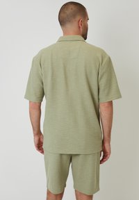 Hellgrünes Polohemd mit kurzen Ärmeln und Kragen, strukturierter Stoff und lockere Passform, kombiniert mit passender Shorts in der gleichen Farbe.