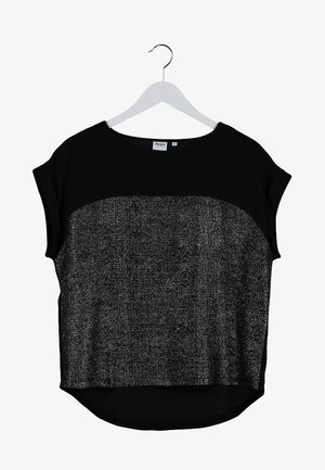 Kvinde iført en sort og sølvfarvet kortærmet top, mørke skinny jeans, sorte ankelstøvler og holder en sort læder crossbody taske.