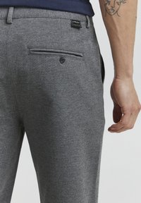 Grey, textured trousers with a back pocket and button closure. Features a small brand label at the waistband. Smooth fabric finish.