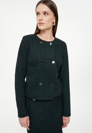 Chaqueta texturizada en verde oscuro con un patrón a cuadros. Presenta un diseño de doble botonadura y botones negros redondos. Silueta ajustada.
