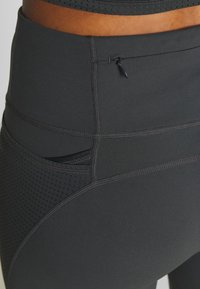 Czarne legginsy z wysokim stanem, wykonane z elastycznego materiału, z boczną kieszenią, dekoracyjnymi szwami i teksturowanymi panelami dla lepszej wentylacji.