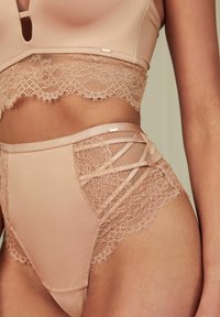 Beha en hoogtaille briefset in lichtbeige, met kantafwerking, ingewikkelde uitsparingen en een zachte stoftextuur. Accenten zijn kleine hardwaredetails.