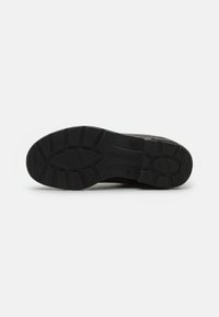 Semelle en caoutchouc noir avec un design texturé et des crevasses profondes pour une meilleure adhérence. Logo de la marque imprimé près de la zone du talon.