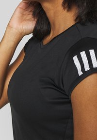 Svart tränings t-shirt med rund halsringning, korta ärmar och tre vita randiga detaljer på axeln. Slät, tight passform i tyg.