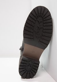 Suela de bota negra con patrón de relieve profundo, material de goma texturizada y marcaje de tamaño "37" sobre una base marrón lisa.
